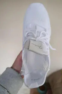 White sneaker with brand logo held by a person wearing gray pants.
